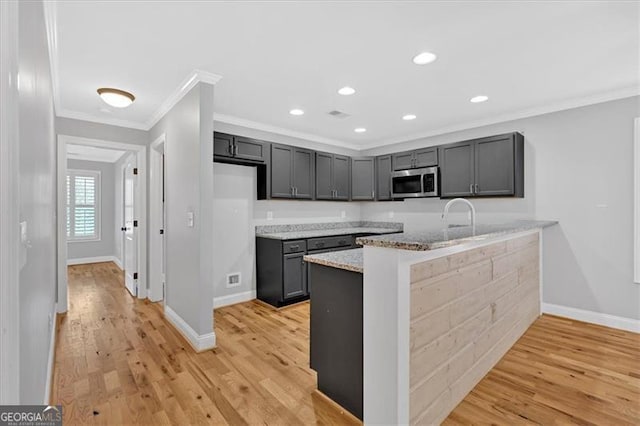 kitchen with light wood-style flooring, crown molding, stainless steel microwave, and light stone counters