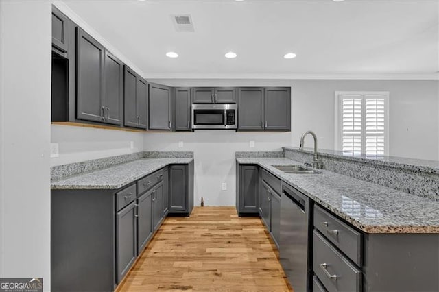 kitchen featuring stainless steel appliances, light wood-style floors, ornamental molding, a sink, and light stone countertops