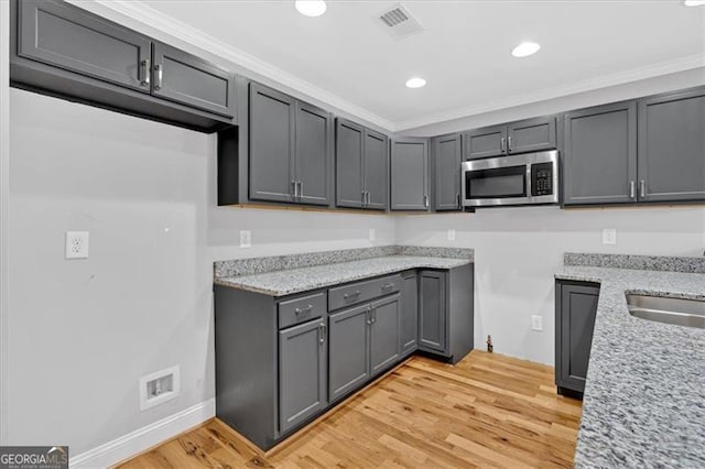 kitchen with light stone counters, light wood-type flooring, stainless steel microwave, and visible vents