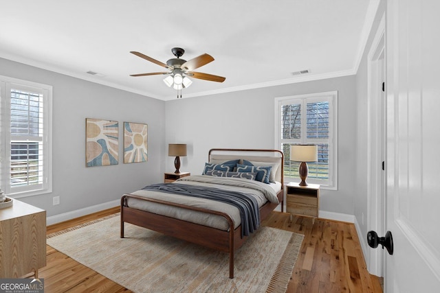 bedroom with baseboards, visible vents, crown molding, and light wood finished floors