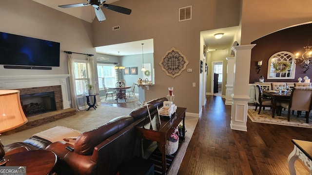 living area with decorative columns, a fireplace, visible vents, wood finished floors, and ceiling fan with notable chandelier