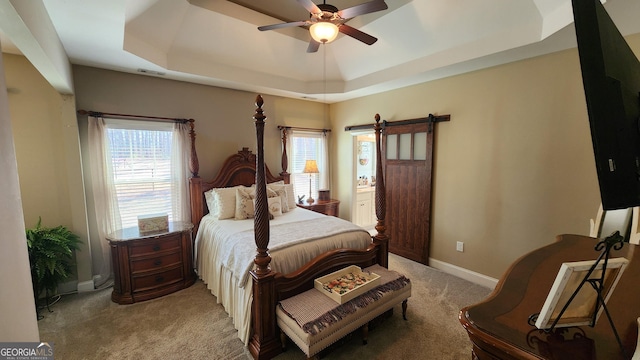 bedroom with a raised ceiling, light colored carpet, a barn door, ceiling fan, and baseboards