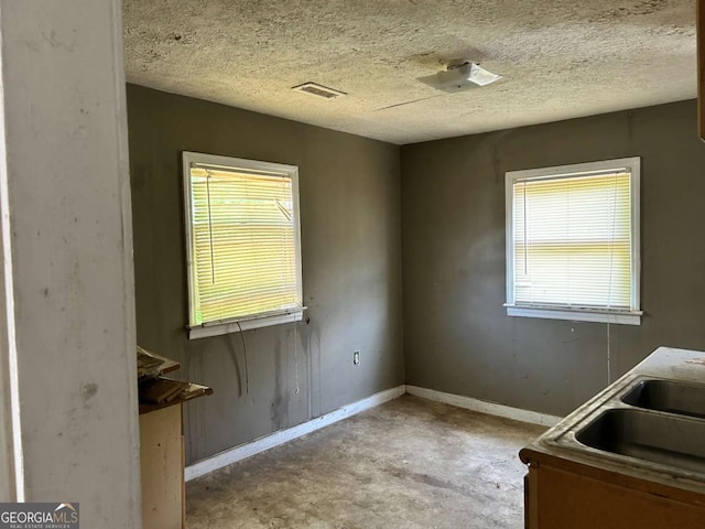 kitchen featuring baseboards, visible vents, a textured ceiling, concrete floors, and a sink