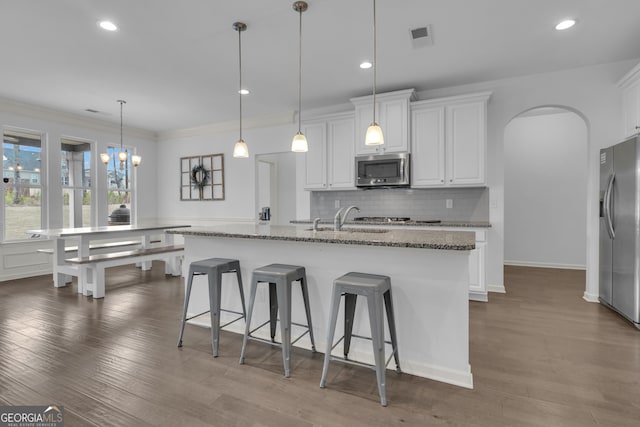 kitchen featuring arched walkways, white cabinets, appliances with stainless steel finishes, a sink, and backsplash