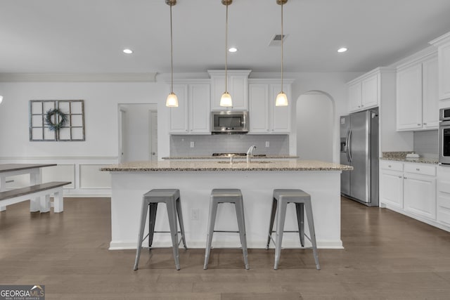 kitchen with arched walkways, appliances with stainless steel finishes, a kitchen island with sink, white cabinetry, and a sink