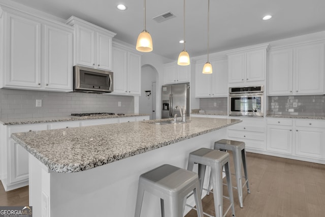 kitchen with stainless steel appliances, arched walkways, white cabinets, and a sink