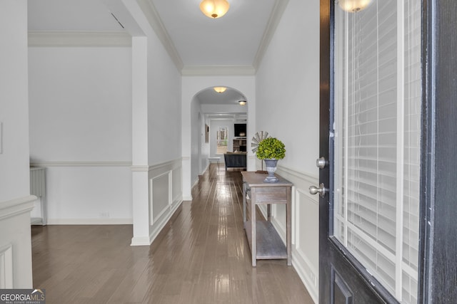 entryway with arched walkways, a decorative wall, crown molding, and wood finished floors