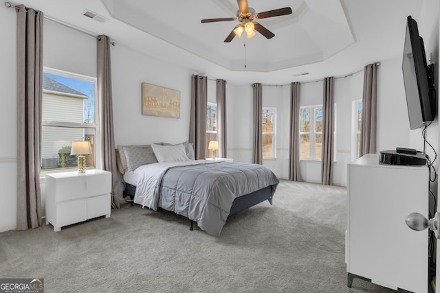 bedroom featuring ceiling fan, a raised ceiling, visible vents, and light colored carpet