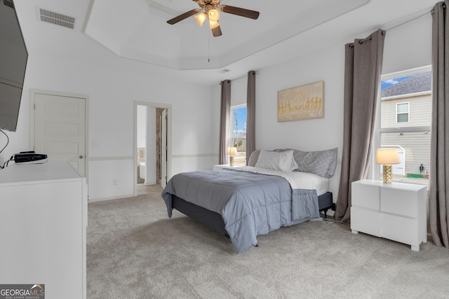 bedroom with a tray ceiling, multiple windows, visible vents, and light colored carpet