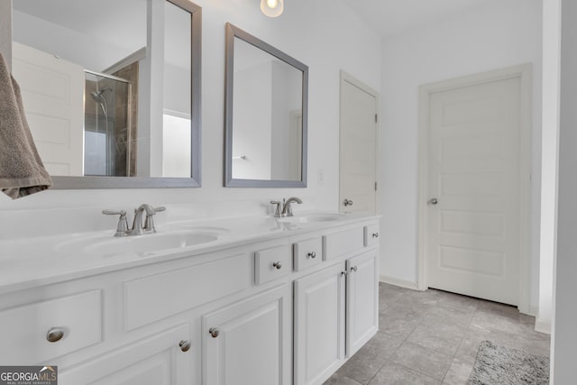 full bathroom with double vanity, tiled shower, a sink, and baseboards