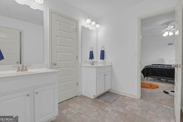 full bath with baseboards, a ceiling fan, stone finish floor, a sink, and two vanities