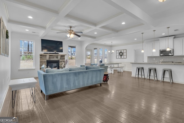 living area with coffered ceiling, dark wood-type flooring, beam ceiling, and a stone fireplace