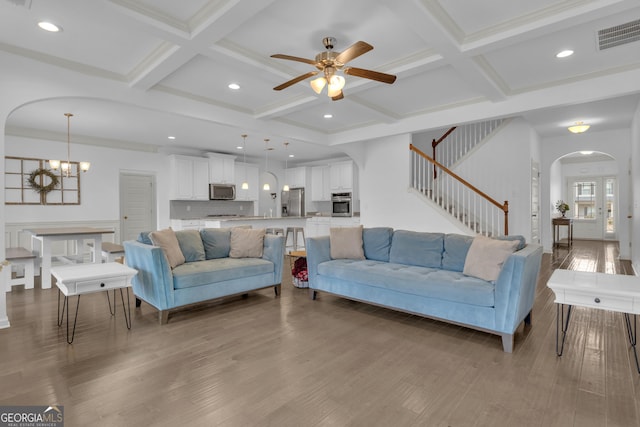 living room featuring arched walkways, visible vents, light wood-style floors, stairway, and beam ceiling