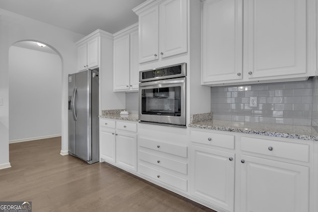 kitchen featuring arched walkways, decorative backsplash, appliances with stainless steel finishes, wood finished floors, and white cabinetry