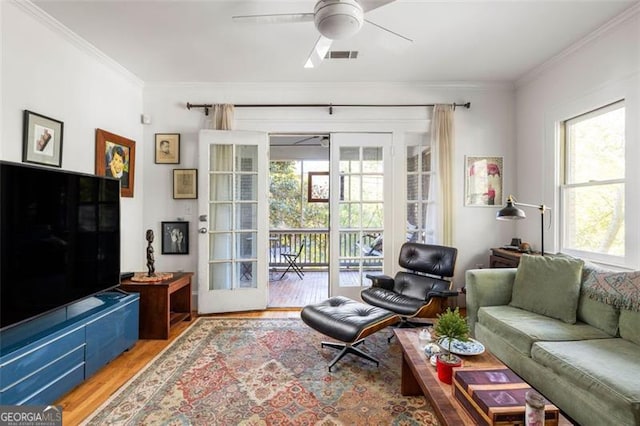 living area featuring a ceiling fan, visible vents, crown molding, and light wood-style flooring