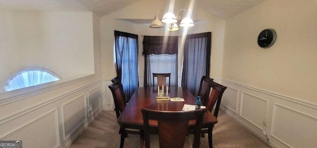 dining room with lofted ceiling, a decorative wall, a notable chandelier, and wainscoting