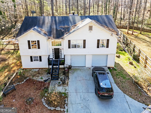 split foyer home featuring a garage, driveway, a chimney, and fence