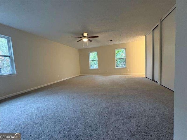 empty room with carpet floors, ceiling fan, a textured ceiling, and baseboards