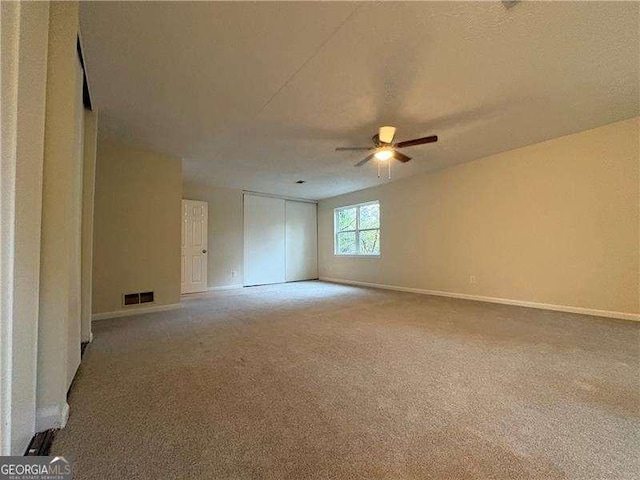 empty room with ceiling fan, carpet floors, visible vents, and baseboards