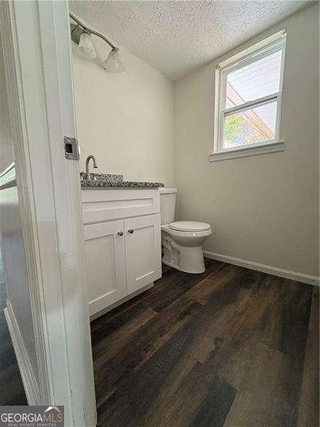 bathroom featuring baseboards, toilet, wood finished floors, a textured ceiling, and vanity