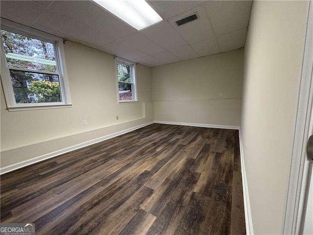 interior space with a paneled ceiling, baseboards, visible vents, and dark wood finished floors