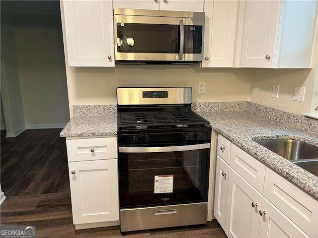 kitchen with light stone counters, dark wood-type flooring, a sink, white cabinets, and appliances with stainless steel finishes