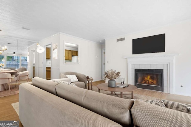 living room featuring a fireplace, light wood finished floors, visible vents, an inviting chandelier, and ornamental molding