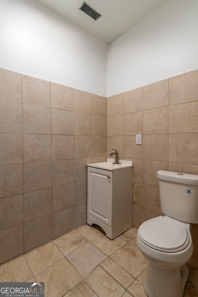 half bath featuring visible vents, tile walls, toilet, and vanity