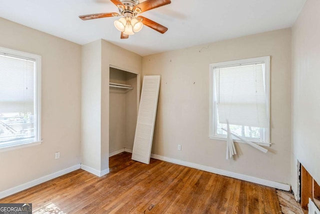 unfurnished bedroom with a closet, multiple windows, wood finished floors, and baseboards