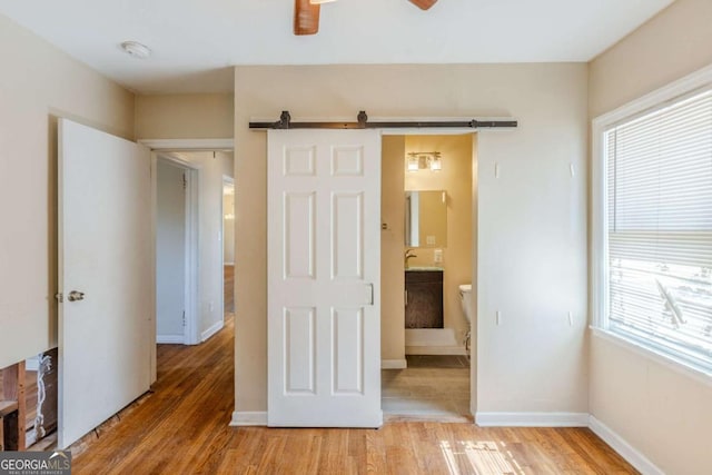 unfurnished bedroom featuring a barn door, baseboards, a ceiling fan, light wood-style flooring, and ensuite bathroom