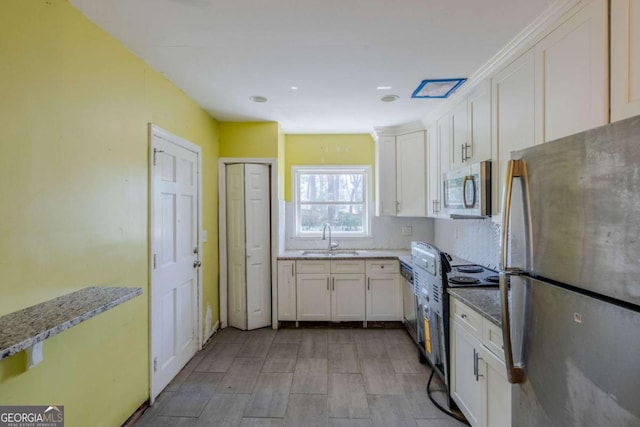 kitchen with stainless steel appliances, white cabinets, a sink, and light stone countertops