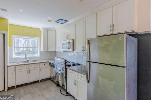 kitchen featuring light stone counters, a sink, white cabinetry, appliances with stainless steel finishes, and decorative backsplash