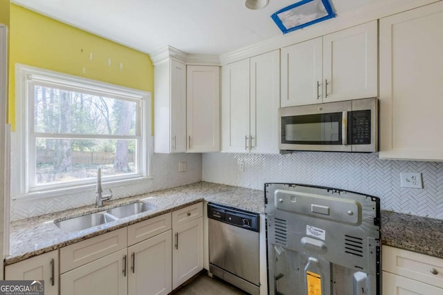 kitchen with backsplash, appliances with stainless steel finishes, white cabinets, a sink, and light stone countertops