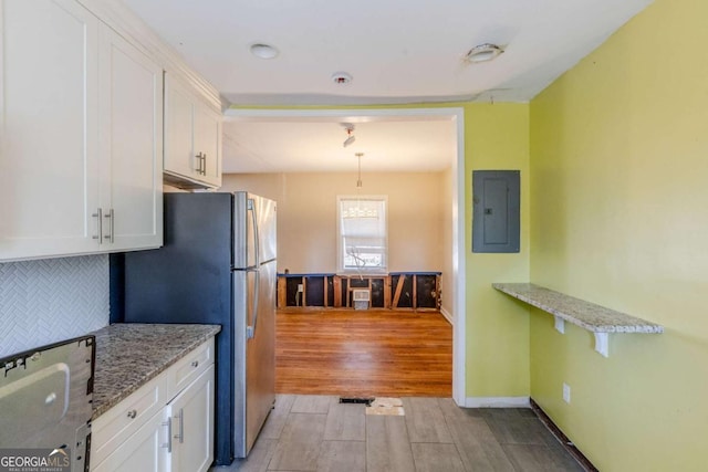 kitchen with electric panel, white cabinets, decorative backsplash, light stone counters, and freestanding refrigerator