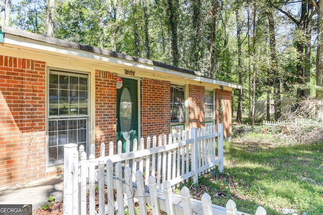 doorway to property with covered porch, brick siding, and fence