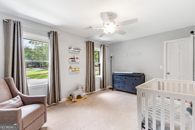 bedroom featuring light carpet, a nursery area, a ceiling fan, and baseboards