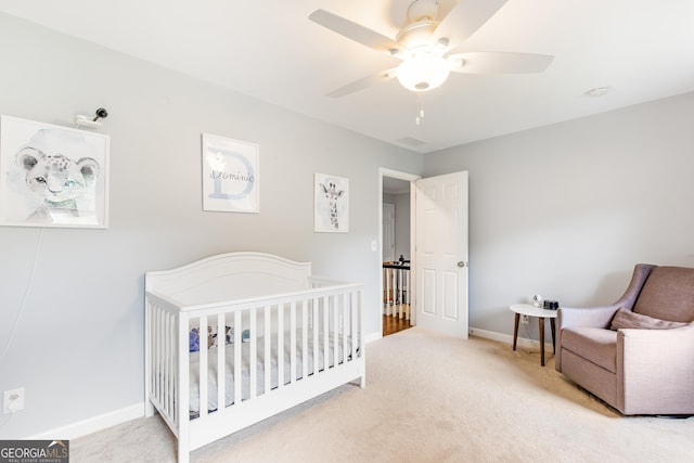 bedroom with a nursery area, carpet, baseboards, and a ceiling fan