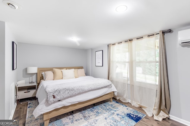 bedroom featuring an AC wall unit, wood finished floors, and baseboards