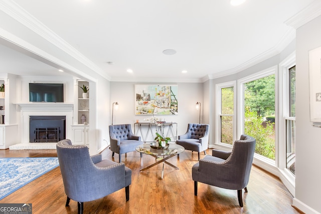 living area with built in features, a glass covered fireplace, ornamental molding, wood finished floors, and recessed lighting