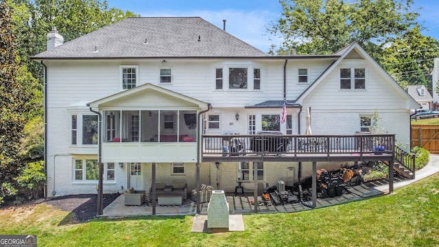 rear view of property featuring a patio, a chimney, a lawn, a sunroom, and a wooden deck