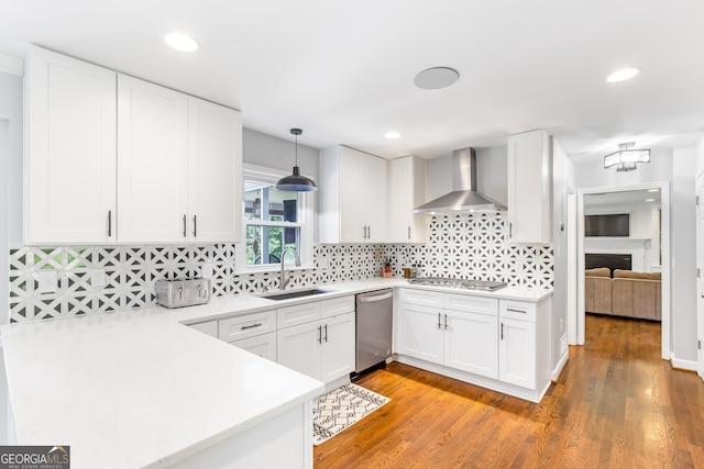 kitchen with wall chimney exhaust hood, appliances with stainless steel finishes, light countertops, white cabinetry, and a sink