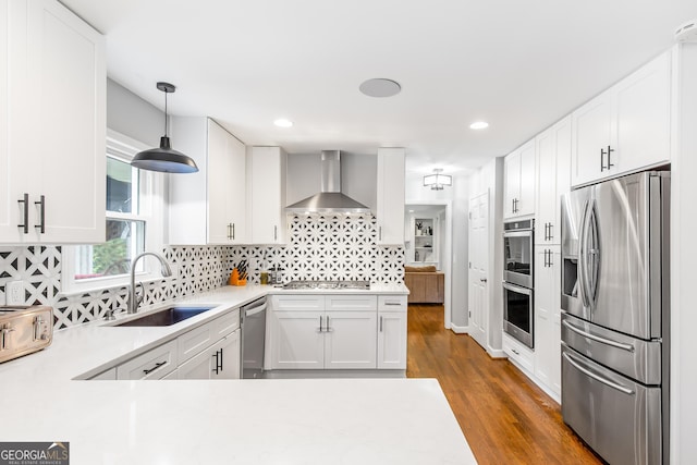 kitchen with white cabinets, wall chimney exhaust hood, appliances with stainless steel finishes, light countertops, and a sink