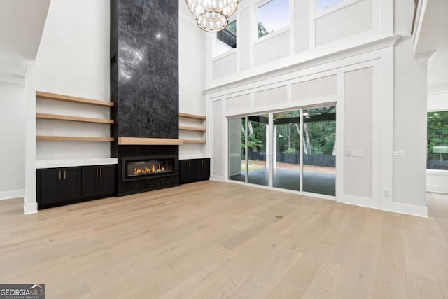 unfurnished living room with a fireplace, a towering ceiling, baseboards, light wood-style floors, and an inviting chandelier