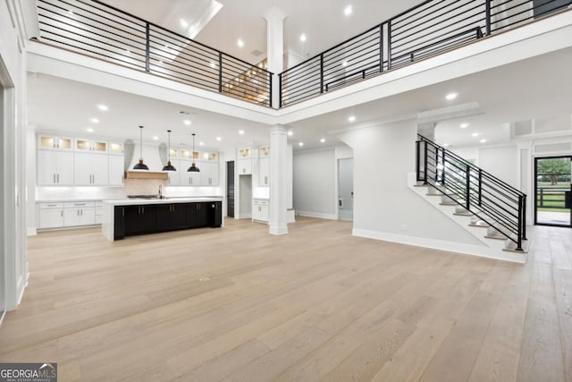 unfurnished living room with decorative columns, baseboards, a high ceiling, stairs, and light wood-style floors