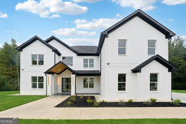 modern inspired farmhouse featuring brick siding, a front yard, and fence