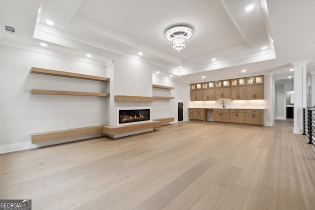 unfurnished living room with light wood-style flooring, visible vents, a raised ceiling, and a glass covered fireplace