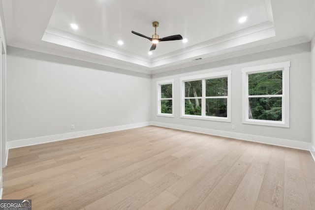 empty room featuring ornamental molding, a raised ceiling, light wood-style floors, and baseboards