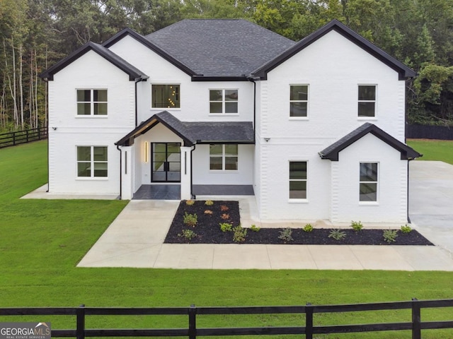 modern farmhouse with a shingled roof, a front yard, and fence