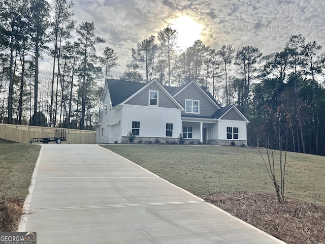 view of front of house with board and batten siding, concrete driveway, stone siding, and a front lawn