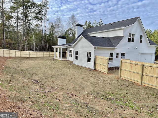 rear view of house featuring a shingled roof, a chimney, and fence